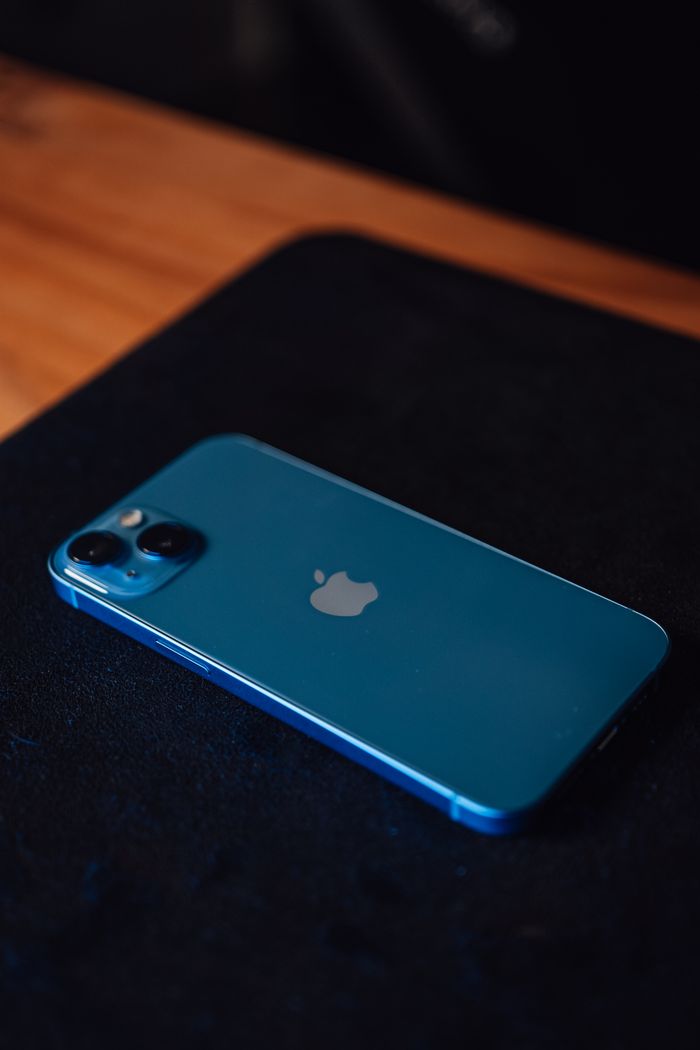 services-03 Close-up of a blue smartphone lying on a black surface with a wooden texture background.